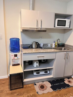 A kitchen with white cabinets, a microwave, a water dispenser, a kettle, and a toaster. - Cozy 1-bedroom condo in marvelous Lapu-Lapu with AC (Lapu-Lapu)