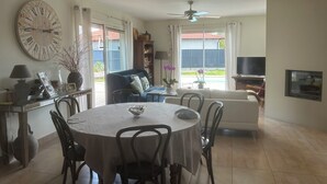 Een eetgedeelte met een ronde tafel, stoelen, een klok en een televisie op de achtergrond.