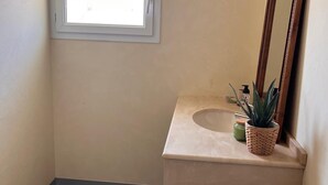 Een badkamer met een raam, een wastafel, een spiegel en een plant in pot.