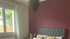 Een slaapkamer met een bed, nachtkastje, lamp, raam met gordijnen en een hanglamp.