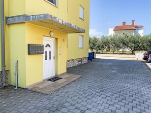 A yellow building with a white door, a small window, and a paved driveway. - Große Ferienwohnung in Ližnjan mit Offenem Kamin by Interhome (Medulin/Ližnjan)