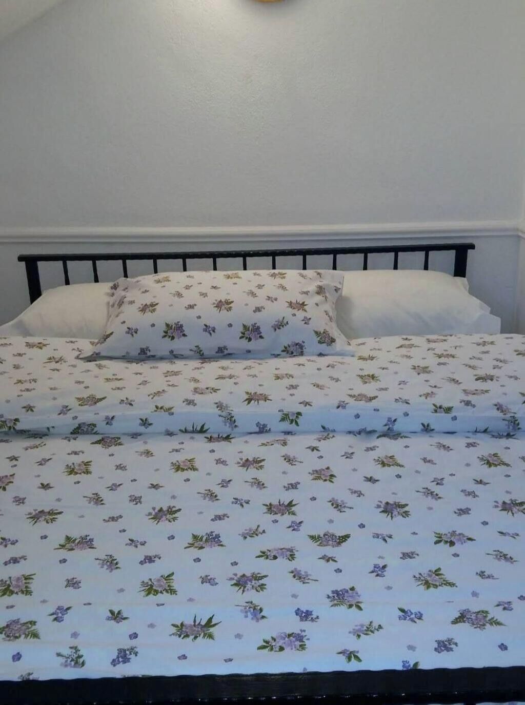 A bed with floral bedding, a black metal headboard, and white pillows.