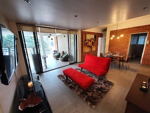 A modern living room with a red sofa, a glass door leading to an outdoor area, and a dining area with a brick wall. - Apartment with terrace, Polanco near Chapultepec forest (Ciudad de México)