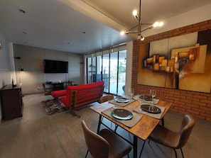 A modern living room with a dining area, a flat-screen TV mounted on the wall, and a large window. - Apartment with terrace, Polanco near Chapultepec forest (Ciudad de México)