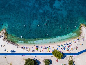 An aerial view of a beach with clear turquoise waters, a sandy shore, and numerous colorful umbrellas and beach chairs. - Villa Rampic by Interhome (Fažana)