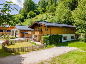 A wooden chalet with a balcony, surrounded by lush greenery and a gravel path. - Comfortable apartment opposite Skilift (Maria Alm)