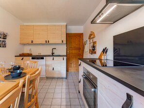 A modern kitchen with wooden cabinets, a built-in oven, and a dining area with a table and chairs. - Comfortable apartment opposite Skilift (Maria Alm)