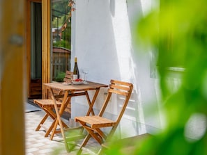 Une table et des chaises en bois sur un balcon, avec une bouteille de vin et un saladier de fruits.