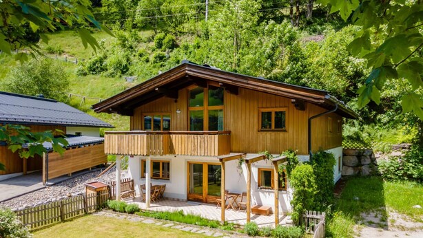 A wooden chalet with a balcony, a stone pathway, and a garden.