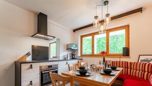 A modern kitchen with a dining area, a red sofa, and a window with a view of greenery.