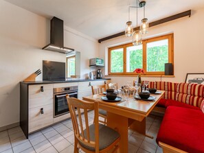 A modern kitchen with a dining area, a red sofa, and a window with a view of greenery. - Comfortable apartment opposite Skilift (Maria Alm)