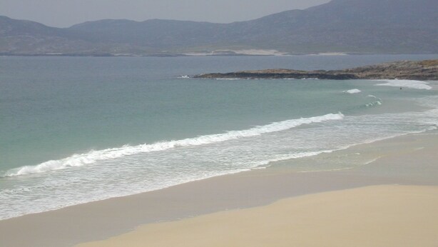 Ein Strand mit klarem Wasser, sandigem Ufer und Bergen in der Ferne.