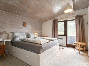 A bedroom with a bed, bedside tables, a lamp, a window with curtains, a wicker chair, and a sun decoration on the wall. - Family Lodge in Kirchberg, 300m to the ski lift (Kirchberg in Tirol)