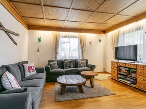 A living room with a sofa, a coffee table, a TV, and a wooden cabinet with games. - Family Lodge in Kirchberg, 300m to the ski lift (Kirchberg in Tirol)