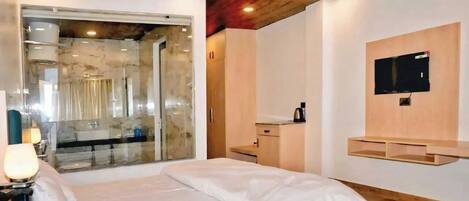 A modern hotel room with a bed, a TV, a wooden ceiling, and a glass door leading to a bathroom.