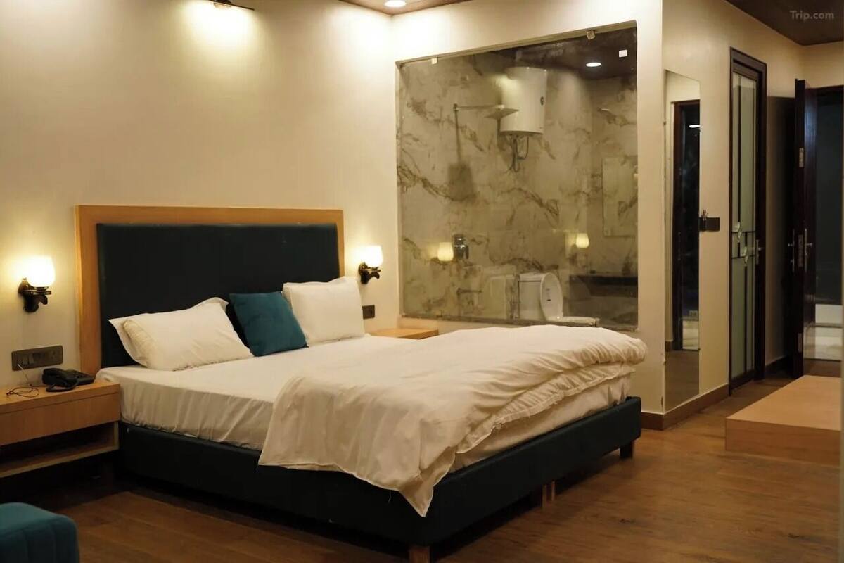 A modern bedroom with a large bed, bedside lamps, a nightstand, and a glass shower enclosure.