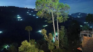 Une vue nocturne d’une région montagneuse, parsemée de lumières, d’arbres et d’un bâtiment en construction.