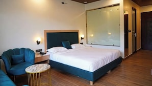 Une chambre d’hôtel moderne comprenant un lit, un coin salon avec un fauteuil et une petite table, une table de chevet et un grand miroir.