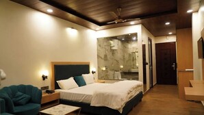 Une chambre d’hôtel moderne comprenant un lit, un coin salon, une salle de bain avec une douche en verre et un plafond en bois.