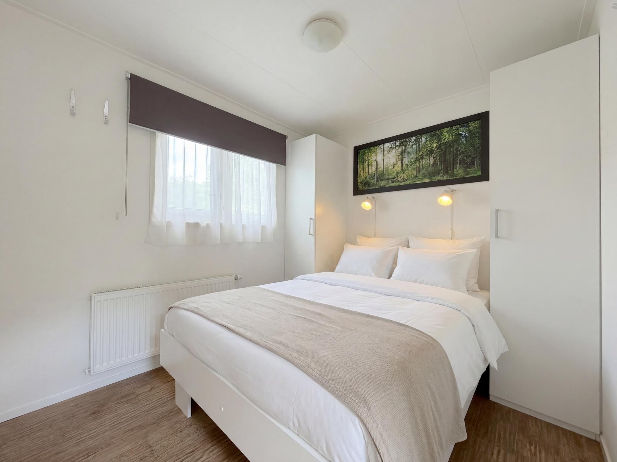 Ein Schlafzimmer mit Bett, einem Fenster mit Vorhängen, einer Heizung, einem Bild an der Wand und einer Deckenleuchte.