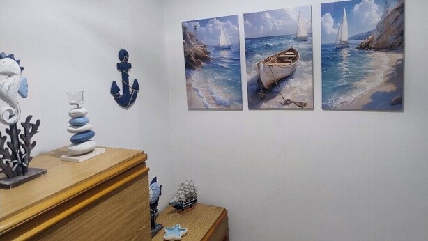 Una stanza con un comò in legno, un tavolino con soprammobili e tre quadri raffiguranti vele.