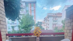 Un patio con tavolo e quattro sedie, un vaso con fiori e vista su edifici sullo sfondo.