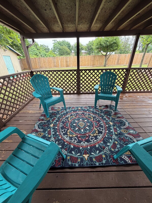 A covered outdoor area with two turquoise Adirondack chairs, a patterned rug, and a wooden deck. - DFW - Big + Private - Nice + New - Cheap Rate! Large groups + Family reunions (Fort Worth)