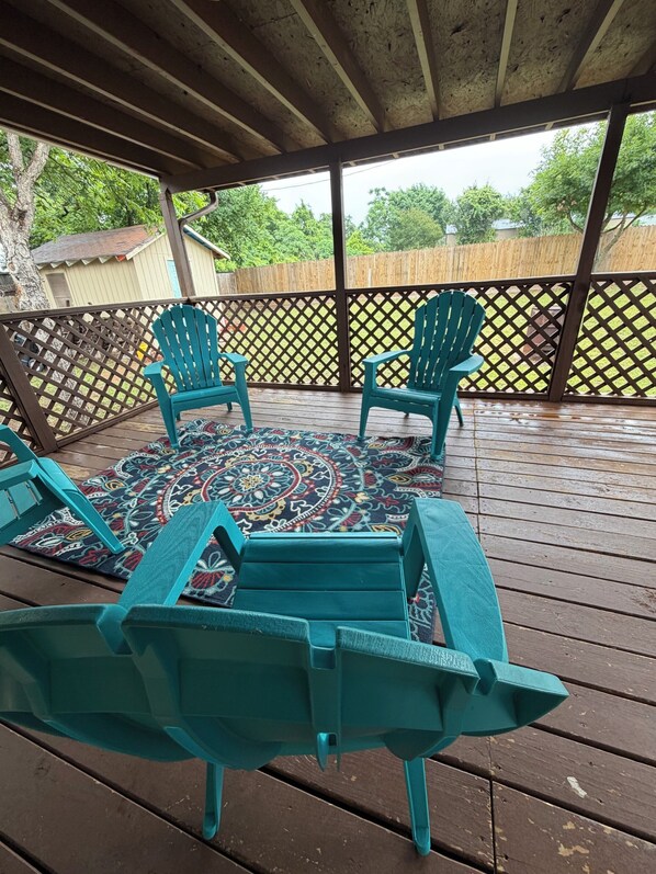 A covered outdoor deck with wooden flooring, a patterned rug, and two turquoise Adirondack chairs. - DFW - Big + Private - Nice + New - Cheap Rate! Large groups + Family reunions (Fort Worth)