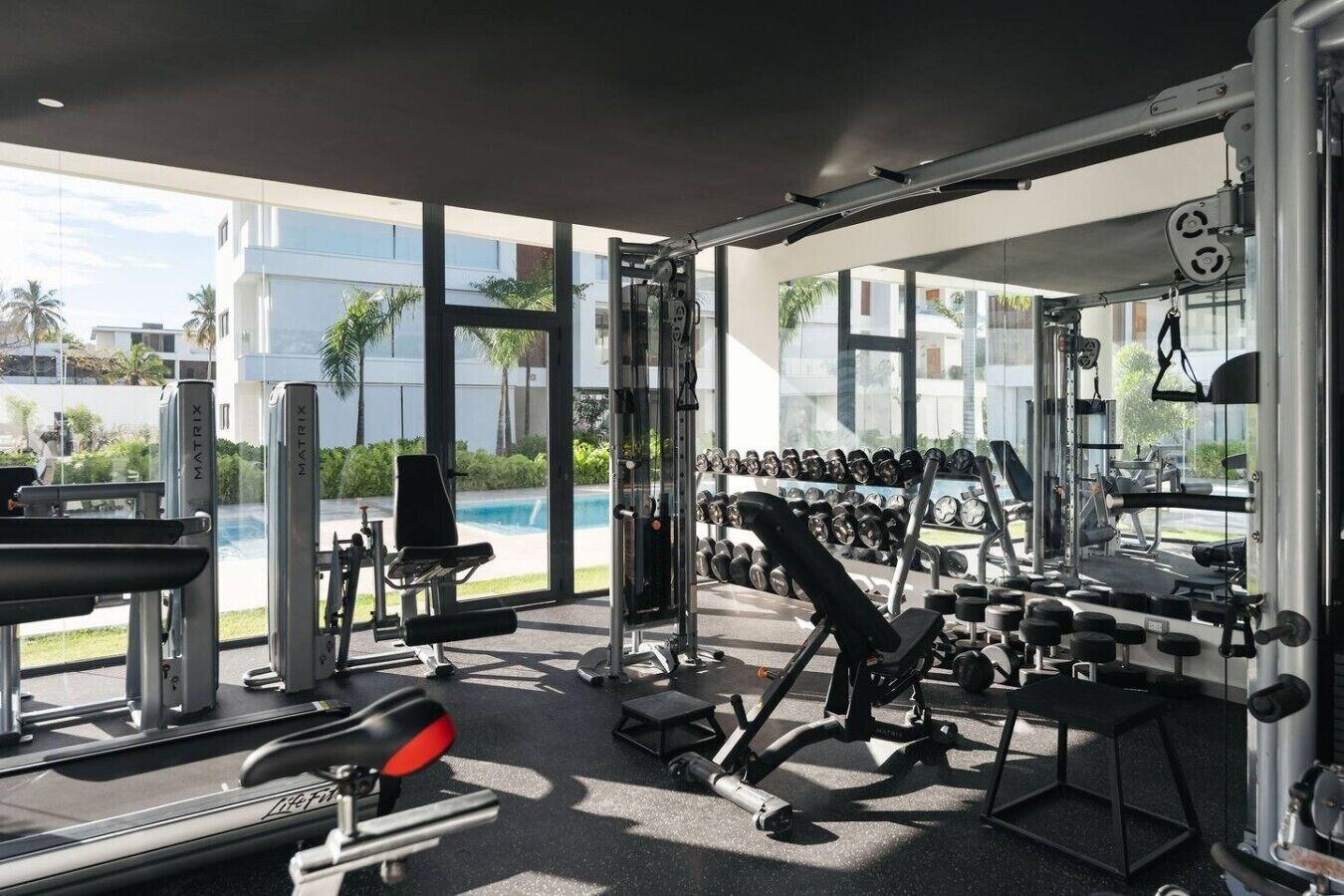 A modern gym with various exercise equipment, a bench, and a rack of dumbbells.