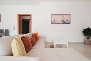 Ein Wohnzimmer mit einer Couch, einer Kaffeemaschine, einem Gemälde von Segelbooten und einer Topfpflanze.