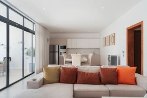 A modern living room with a sofa, a dining area with a table and chairs, and a kitchen in the background. - 2BR/2.5BA Beachfront Condo | Sol de Arena B2 (Las Terrenas)