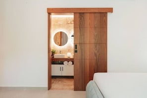 A modern bathroom with a wooden door, a round mirror, a sink, and cabinets. - 2BR/2.5BA Beachfront Condo | Sol de Arena B2 (Las Terrenas)
