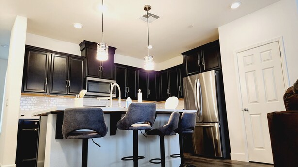 Une cuisine moderne avec des meubles de couleur sombre, des appareils électroménagers en acier inoxydable et des tabourets de bar.