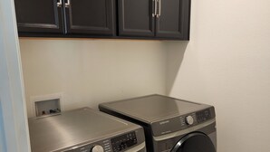 Une buanderie équipée de deux lave-linge Samsung à chargement frontal, avec des meubles de rangement sombres au-dessus et un mur de couleur claire.