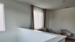 Une pièce avec un mur de séparation blanc, une fenêtre avec des rideaux, une chaise et un sol recouvert d’une moquette.