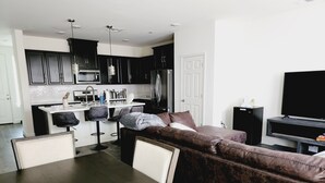Une cuisine moderne avec des meubles de couleur sombre, un plan de travail blanc et un îlot central doté de tabourets de bar.