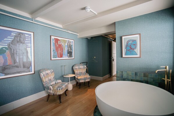 A bathroom with a bathtub, two armchairs, a small table, and framed artwork on the walls. - Gamlekaien (Karmoy)