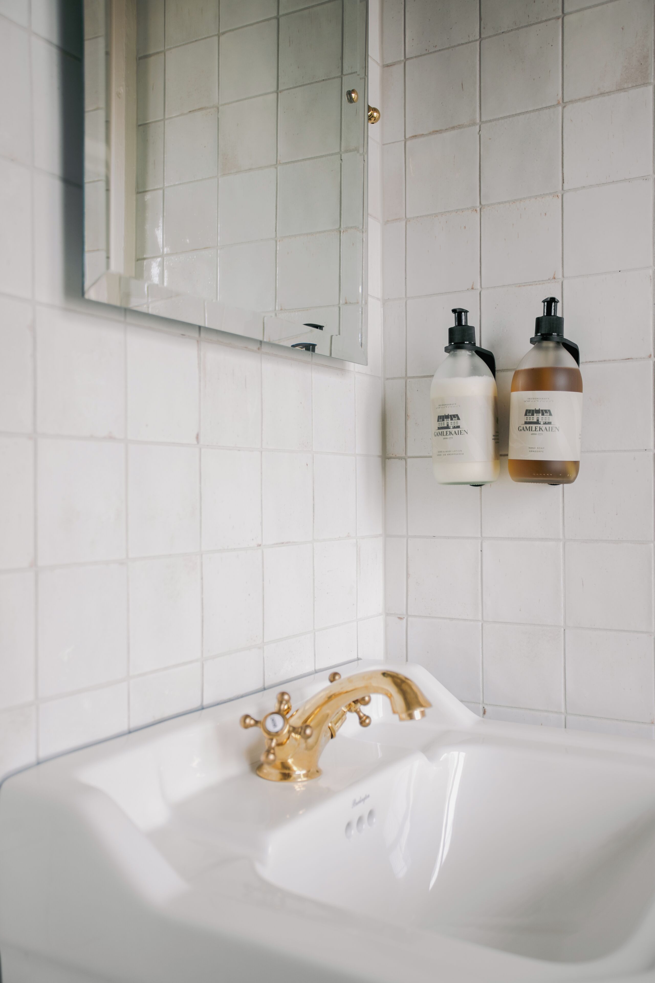 A bathroom with a white sink, gold faucet, and two bottles of lotion on the wall.