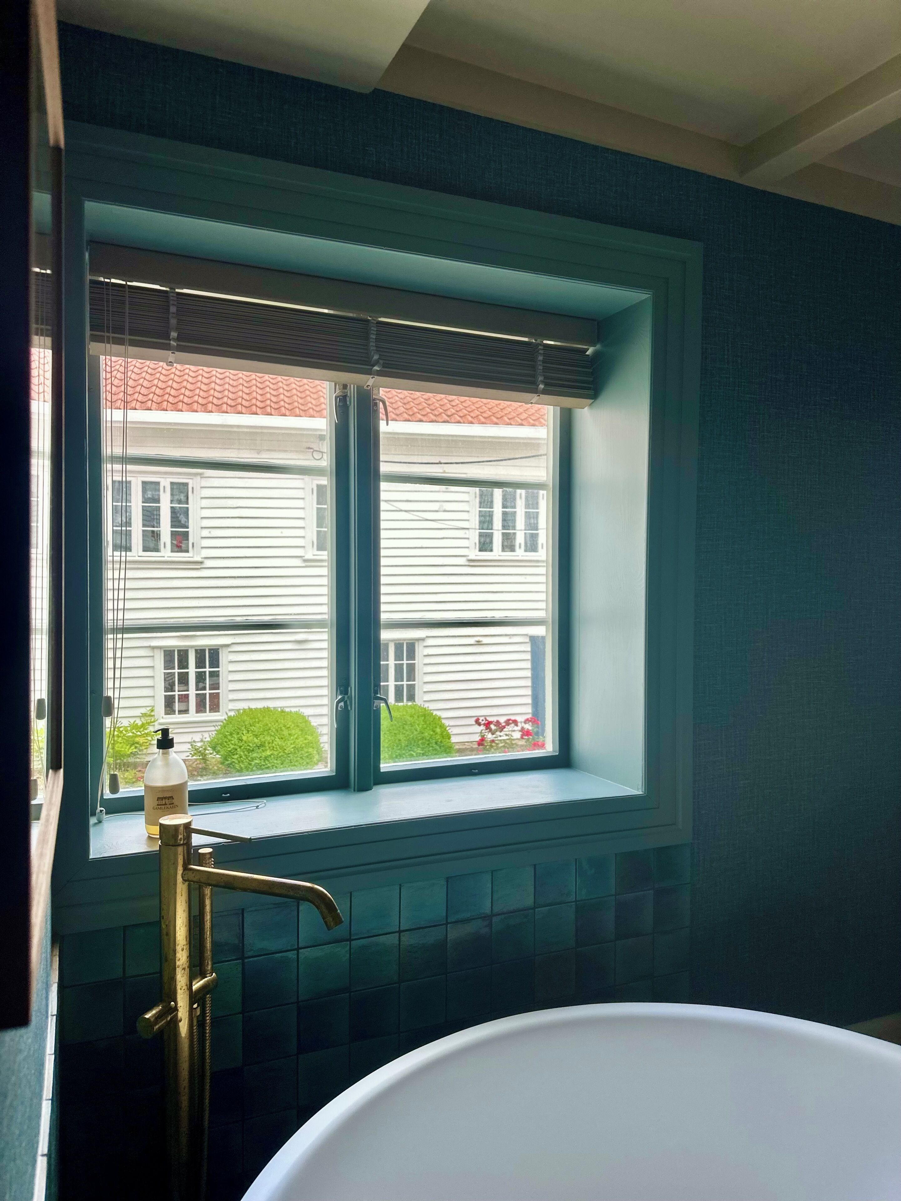 Un baño con bañera, una ventana con vista a una casa y un dispensador de jabón en el alféizar.