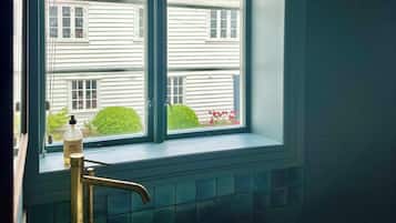 Un baño con bañera, una ventana con vista a una casa y un dispensador de jabón en el alféizar.