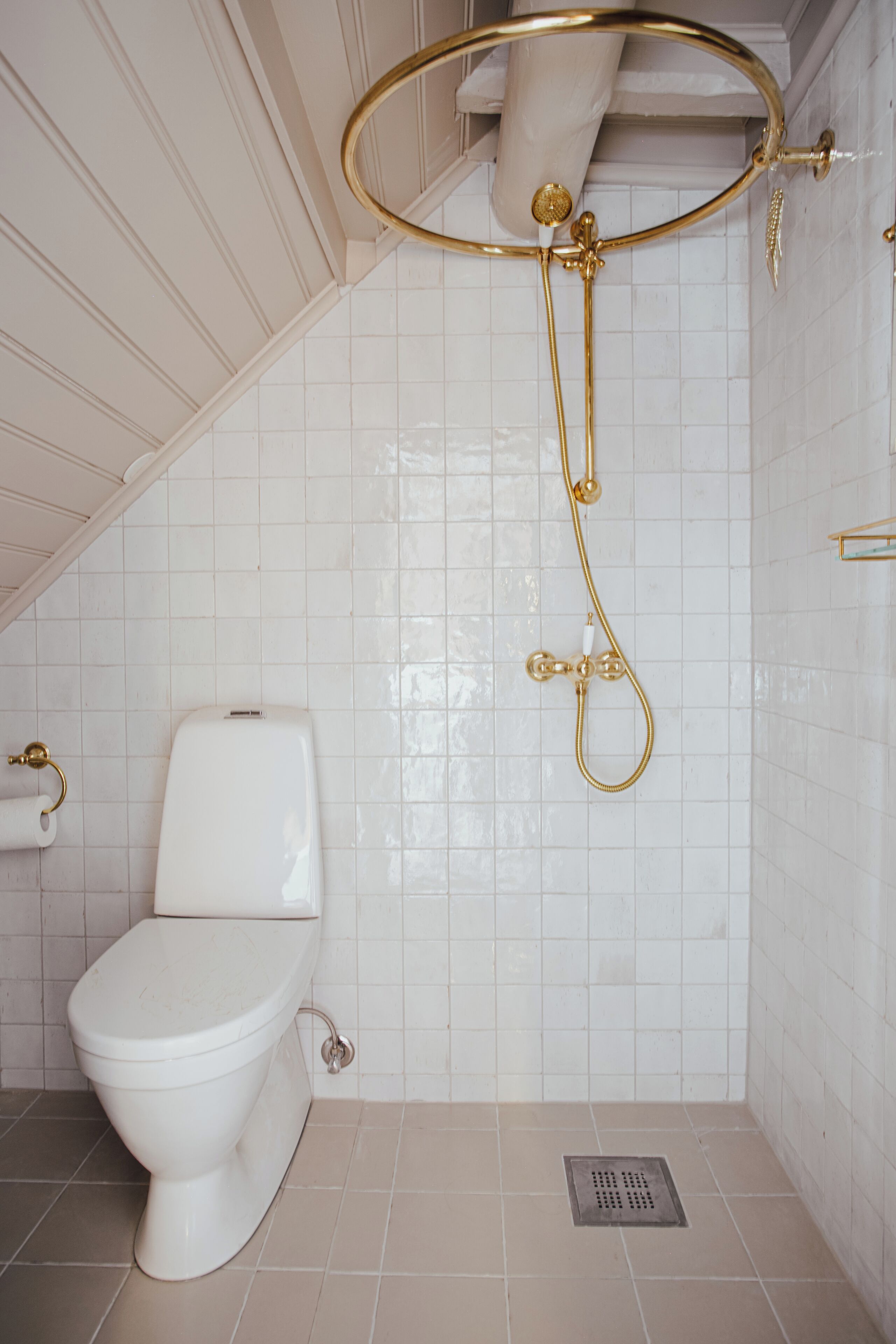 A bathroom with a white toilet, a shower with a gold shower head, and a white tiled wall.