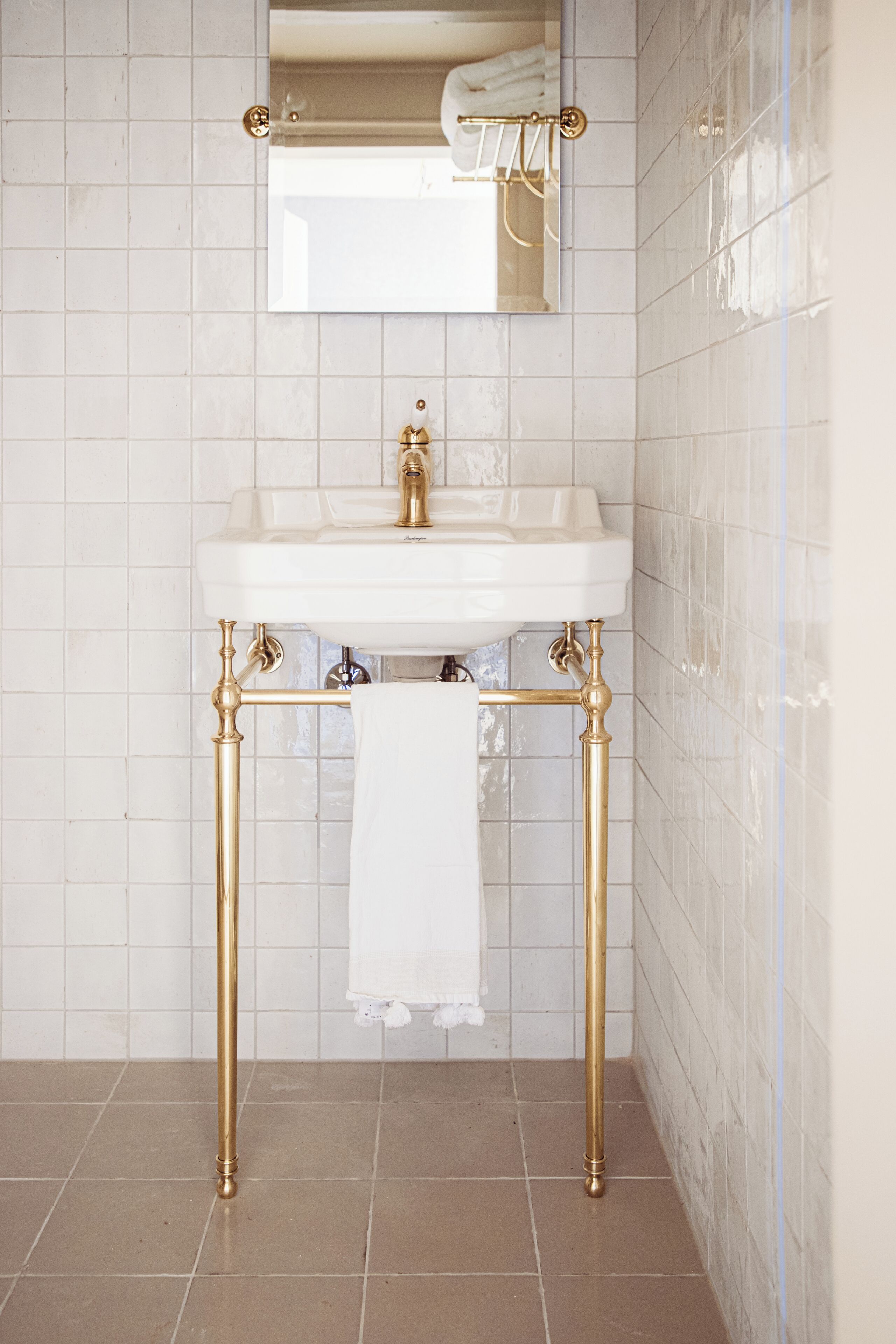 A bathroom with a white sink, gold fixtures, and a mirror above it.
