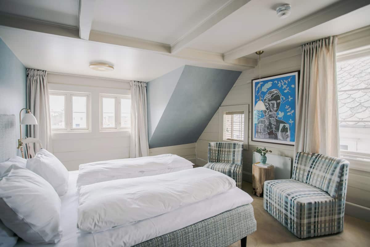 Een hotelkamer met twee bedden, een stoel, een tafeltje en een raam met gordijnen.