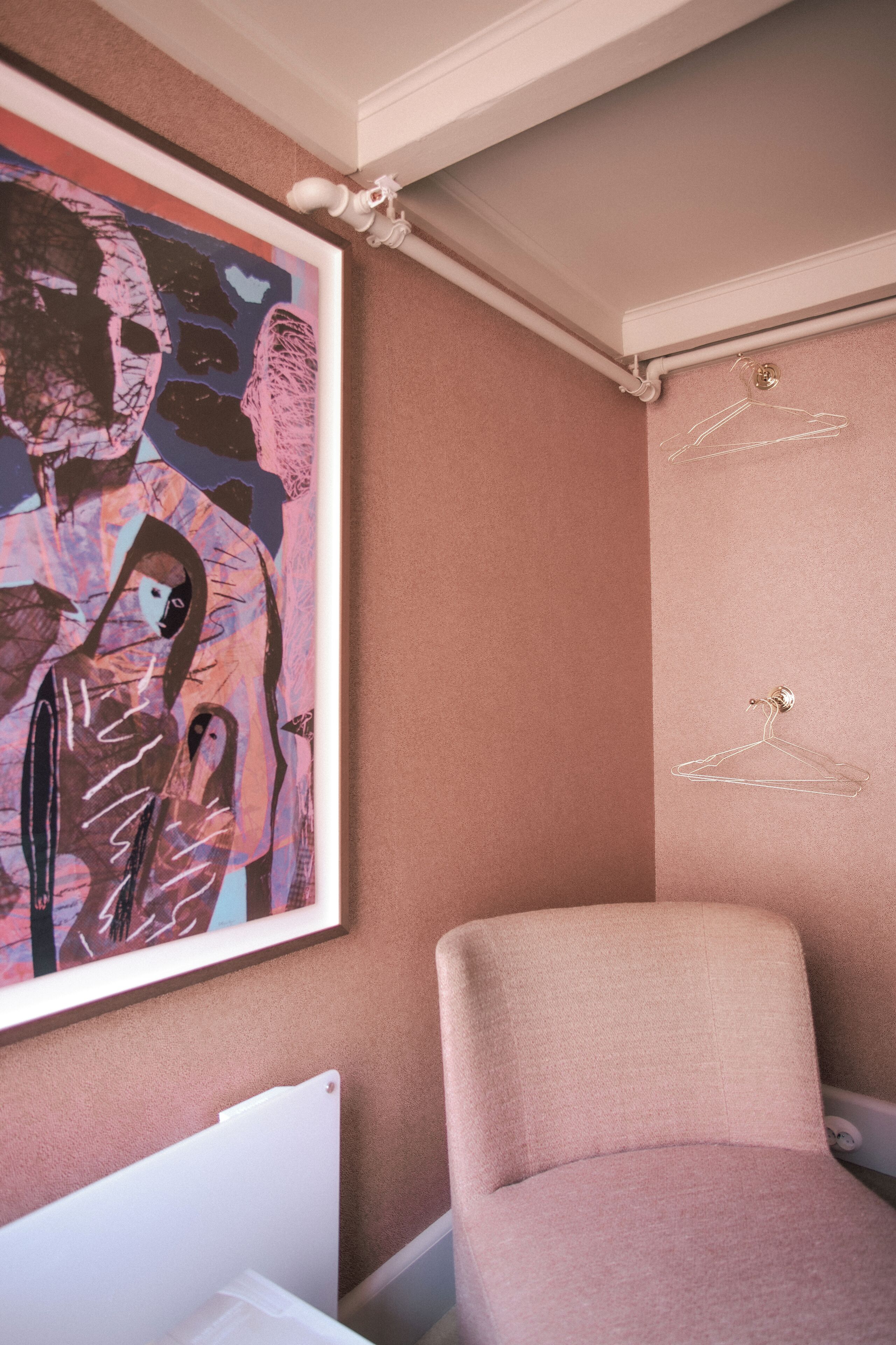 A room with a large abstract painting, a pink chair, and a white radiator.