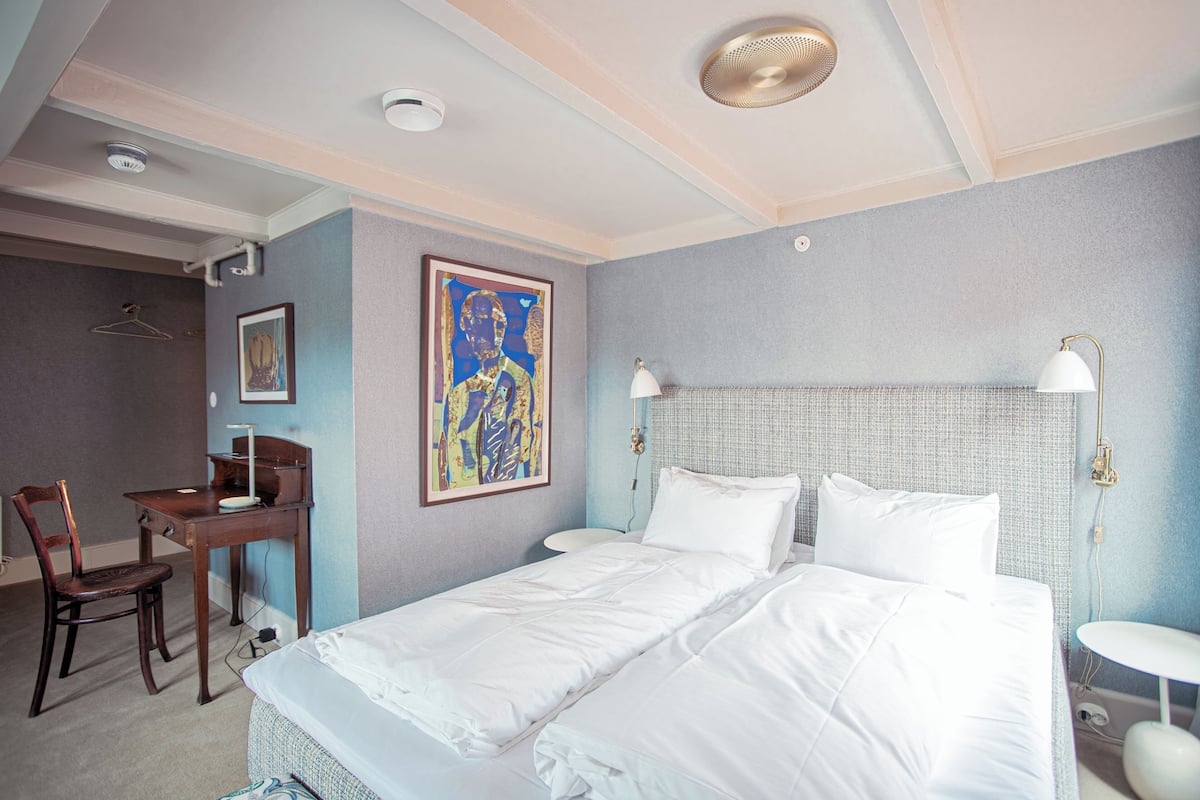Een hotelkamer met een tweepersoonsbed, een bureau met stoel, een schilderij aan de muur en een hanglamp.