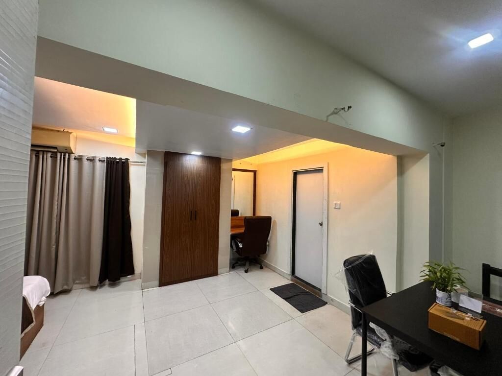 Um quarto com uma cama, uma escrivaninha, uma cadeira, uma pequena mesa com uma planta e uma porta.
