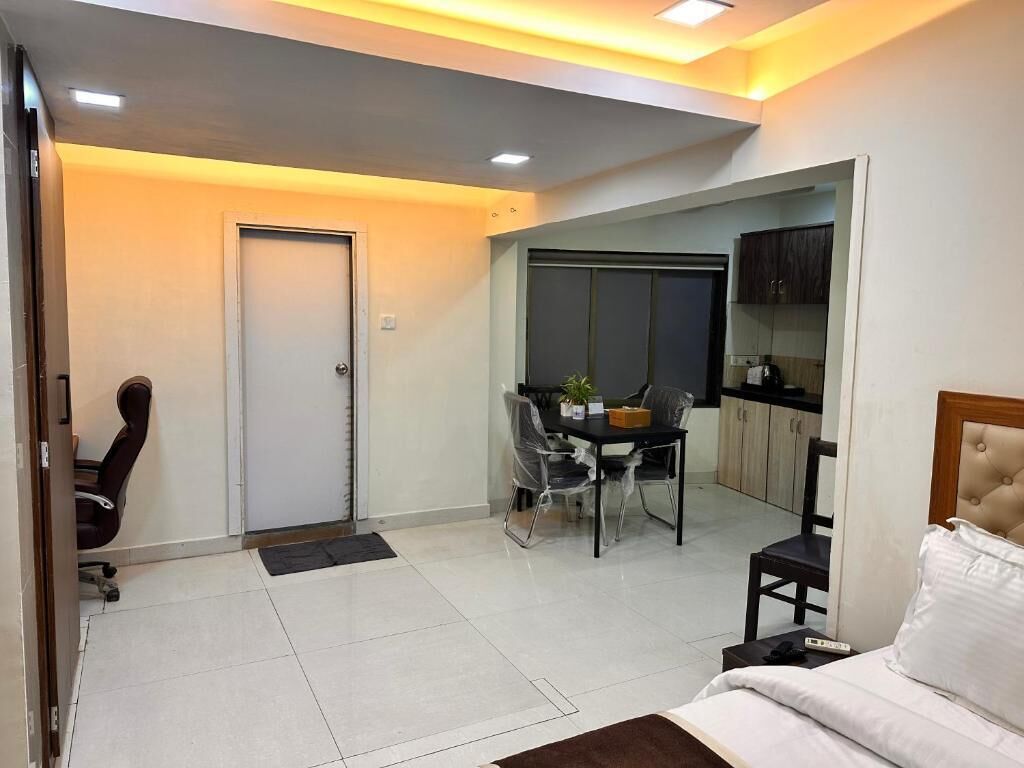 A hotel room with a bed, a desk, a chair, a dining table, and a sliding door leading to a balcony.
