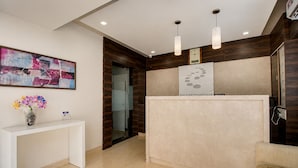 A reception area with a white desk, a vase of flowers, a modern reception desk, and a wall-mounted clock.