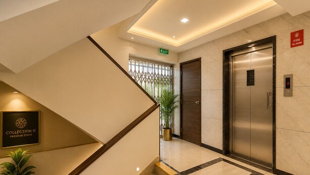 A hotel lobby with a staircase, an elevator, a fire alarm sign, and a 'Collection O Premium Stays' sign.