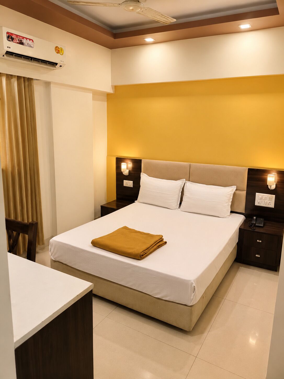 A hotel room with a large bed, bedside tables, an air conditioning unit, and a ceiling fan.